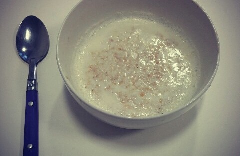A camera down shot of gluten free porridge in a white bowl with a black handled spoon to the right-hand side.