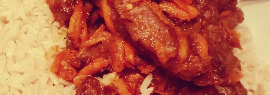 A close up of crispy Szechuan chilli beef on rice in a white bowl with red chopsticks.
